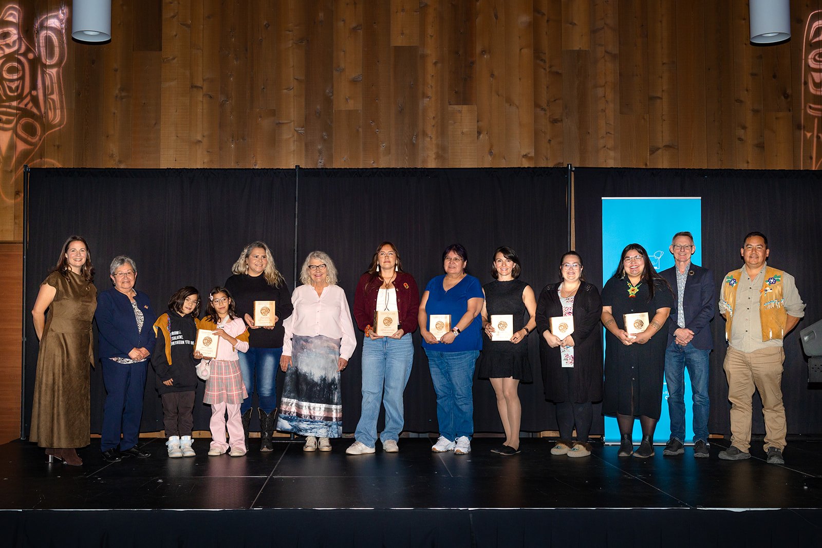 Content providers and presenters stand in a row on stage, several holding wooden award plaques.
